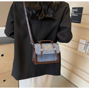 Detail of vintage denim and brown leather crossbody bag with silver butterfly metal buckle