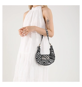 Detail of zebra print crescent bag with metal clasp worn by a model in a white dress