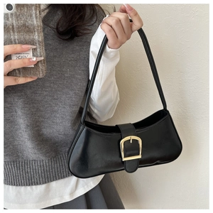 Close-up of black retro shoulder bag with a large gold buckle on minimalist knitwear
