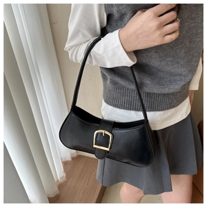 Close-up of a black matte baguette shoulder bag with a gold buckle on a model
