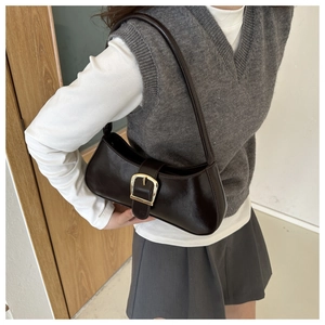 Detail view of deep brown baguette bag with oversized golden buckle on shoulder