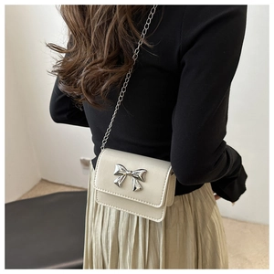 Detail of silver metal bow buckle on a beige mini chain crossbody flap bag for women