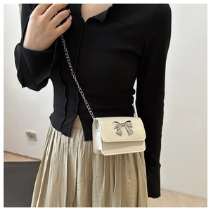 Detailed shot of cream mini crossbody bag with a silver bow clasp on a female model