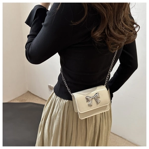 Mini cream crossbody bag with silver bow accent shown on a model for a stylish look