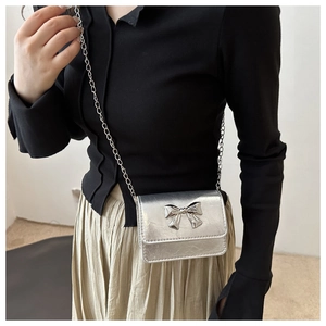 Close-up of mini silver metallic crossbody bag featuring a 3D bow buckle and chain strap