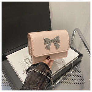 Close-up of pink mini chain bag featuring a large silver metal bow on glossy patent leather