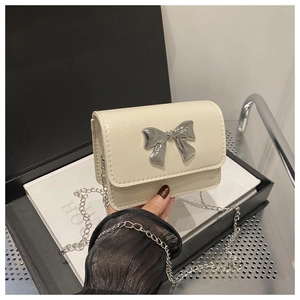 Detail of a creamy white mini square bag with a silver metal bow and fine chain strap