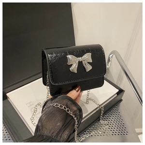 Detail of glossy black patent crossbody bag with a silver metal bow buckle and chain strap
