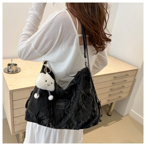 Détail d'un sac cabas plissé noir avec un charm nuage blanc pelucheux porté à l'épaule