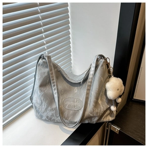 Detail of silver-grey tote bag with crinkled texture, logo plate and white fur ball charm