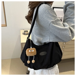 Detail of black nylon tote bag with fashion patch and a cute brown plush monster charm