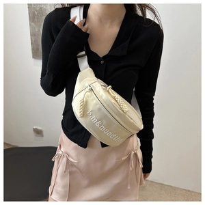 Détail d'un sac bandoulière crème avec broderie de lettres et tirettes tissées