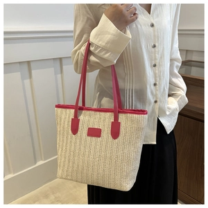 Close-up of woven straw tote bag with bright pink leather handles and trim detail