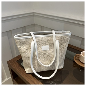 Close-up of beige woven tote bag with white leather straps on a glass table