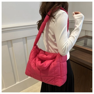 Rose red quilted puffer tote bag with wide straps shown on a model in a minimalist room