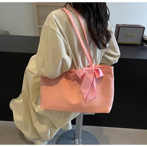 Pink tote bag with plaid ribbon detail shown on model in a modern cafe setting