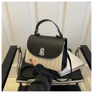 Detail view of the black leather flap with silver metal twist lock on a woven straw bag