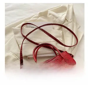 Macro detail of red crocodile pattern handbag with golden text and adjustable strap