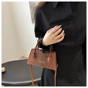 Detailed shot of brown crocodile pattern handbag with dual handles and gold lettering