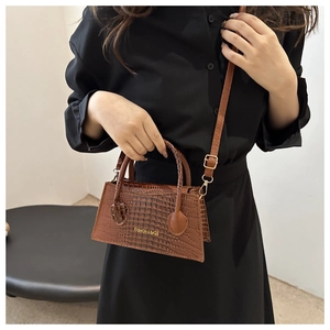 Detail of brown crocodile pattern mini bag with golden hardware and adjustable strap