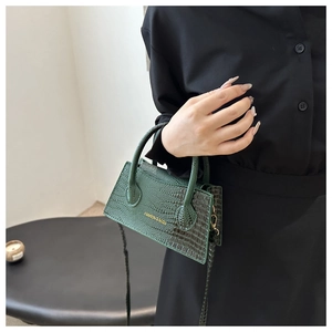 Detailed close-up of dark green crocodile pattern leather handbag with gold metal hardware