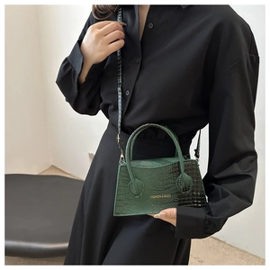 Detail of dark green crocodile texture handbag with gold fashion text and long strap