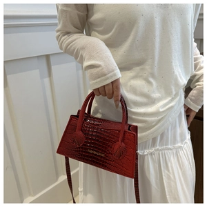 Detail of red croc-embossed leather handbag with gold logo and adjustable shoulder strap