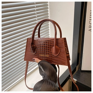 Detail showing brown crocodile pattern handbag with golden embossed logo and fine texture