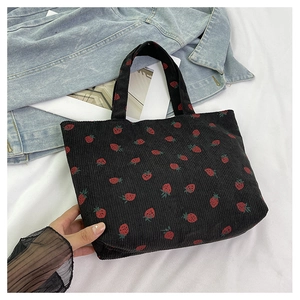 Gros plan du sac cabas en velours côtelé noir avec broderie fraises sur fond denim
