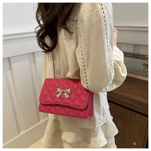 Magenta quilted crossbody bag with silver bow buckle worn on model over white dress