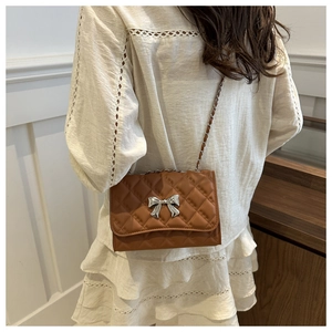 Brown quilted crossbody bag with silver bow detail shown on a model's shoulder