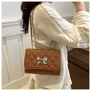 Brown quilted crossbody bag with silver bow accent and chain strap worn by a model