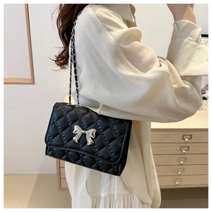 Detail of black quilted leather shoulder bag featuring a silver bow buckle and chain strap