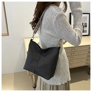 Modern knit bucket bag with wide shoulder strap worn by a model in a minimalist room