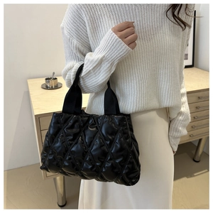 Detail of black quilted puffer handbag featuring glossy material and padded texture