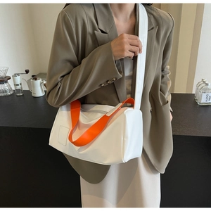 Detail of white cylinder bag with orange handles and wide strap worn by a model