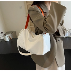 Detail of white leather cylinder bag featuring a vibrant orange shoulder strap