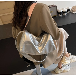 Detail of silver metallic cylinder bag with wide shoulder strap worn by a model