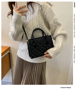 Detail of a black crossbody bag with heart quilted texture on a beige knit sweater