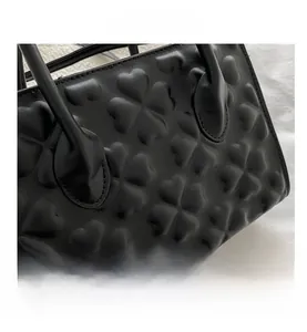 Close-up of black matte faux leather handbag with embossed four-leaf clover texture