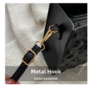 Detail of the golden metal snap hook and embossed pattern on the black leather bag