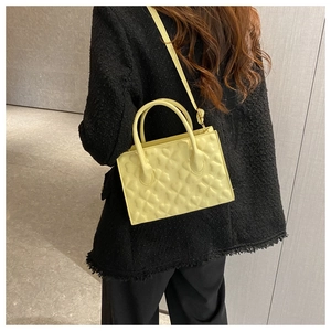 Close-up of cream yellow crossbody bag with heart quilted pattern on black tweed jacket