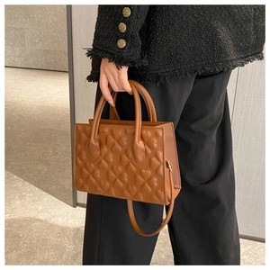 Close-up of caramel clover embossed small square bag held by a model in casual attire