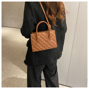 Close-up of caramel brown tote bag featuring embossed heart pattern and gold hardware