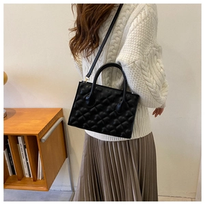 Detailed view of black clover quilted handbag styled with a white knit sweater