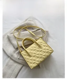 Detail view of yellow crossbody bag featuring embossed floral patterns and top handle