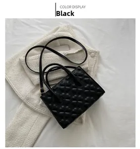 Detail of black vintage handbag with embossed clover patterns and gold hardware on white tweed