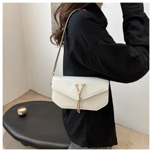 Detail of white envelope shoulder bag featuring a gold V-logo and decorative tassels
