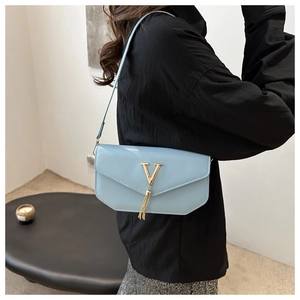 Close-up of light blue shoulder bag with golden V-logo and fringe detail on the model