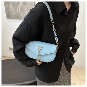 Detail of light blue crossbody bag featuring gold V-logo and decorative tassel accent